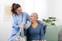 Eine Pflegerin legt einer älteren Frau eine Decke um die Schultern. Das Bild zeigt eine Pflegerin, die einer älteren Frau zu Hause eine Decke um die Schultern.