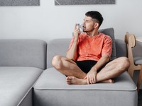 Das Bild zeigt einen Mann, der auf einem Sofa sitzt und inhaliert. 